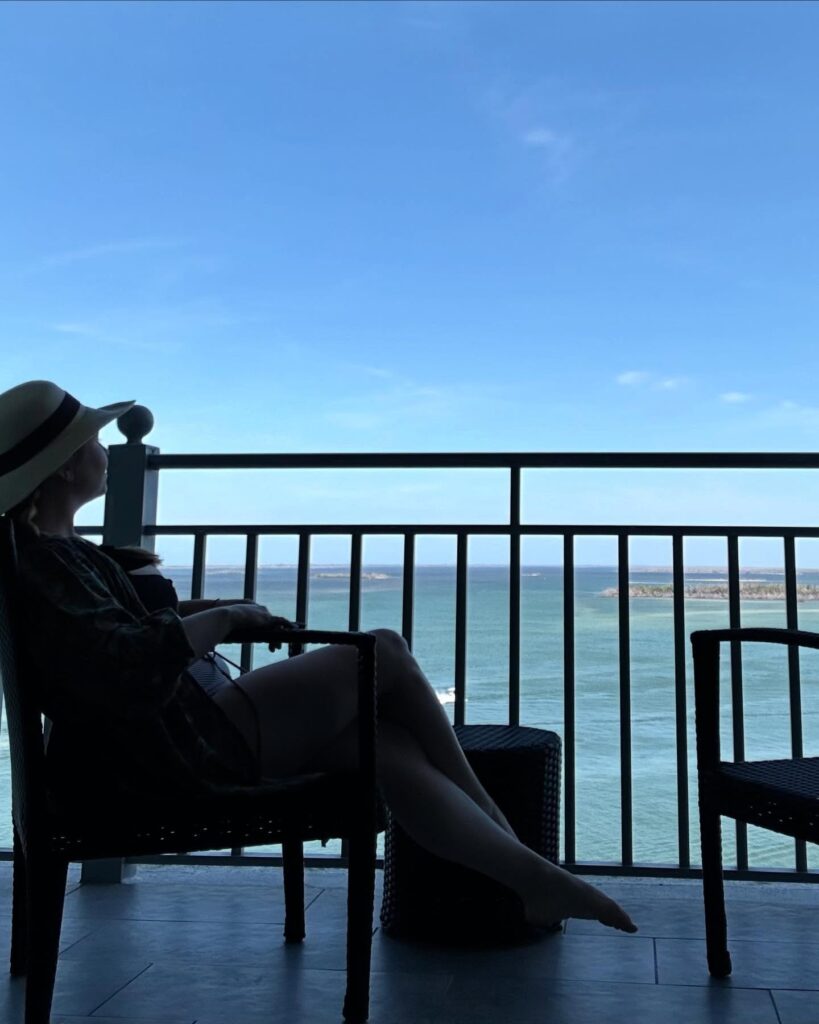 Dr. Jenny Martin sitting in a chair by the ocean, reflecting her love of travel, depth, and contemplation.