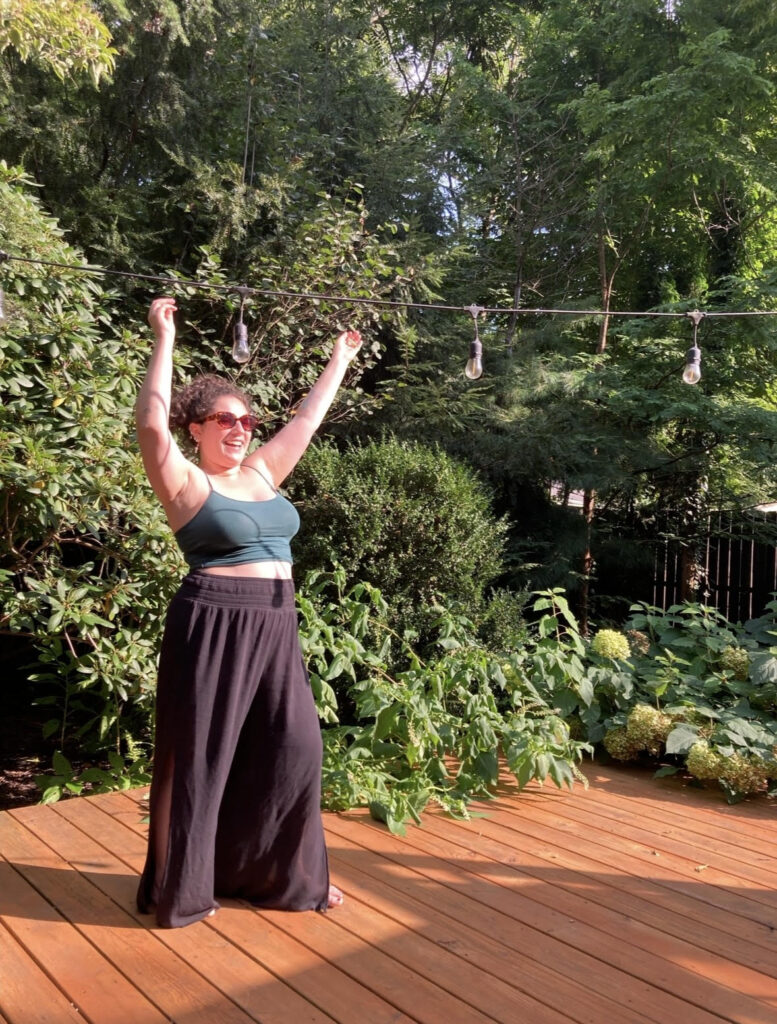 Stef Stone, therapist at Gemstone Wellness, dancing outdoors with sunglasses and a smile.