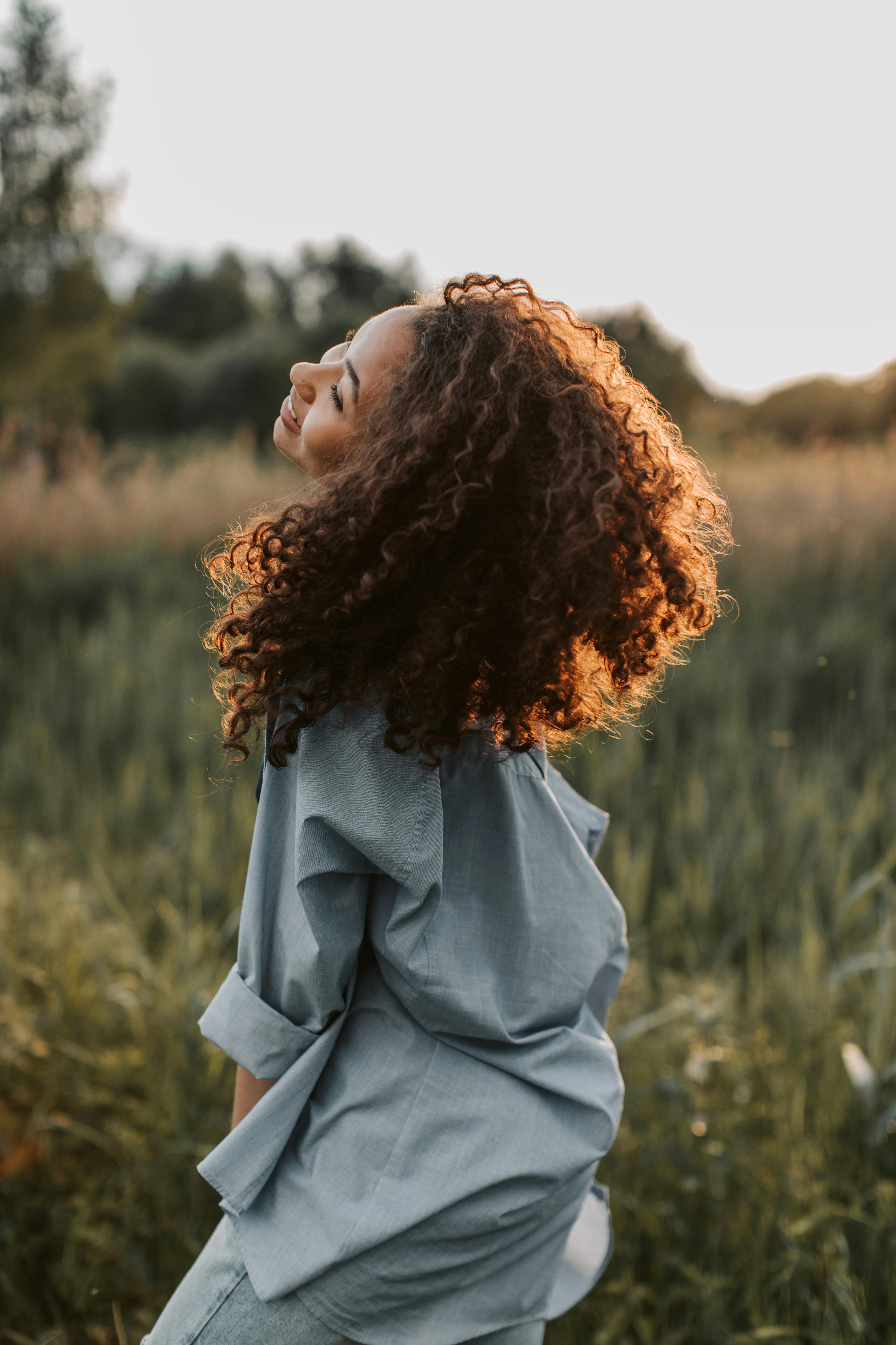 a young woman with curly hair is outside in a meadow smiling after healing from trauma therapy Chicago