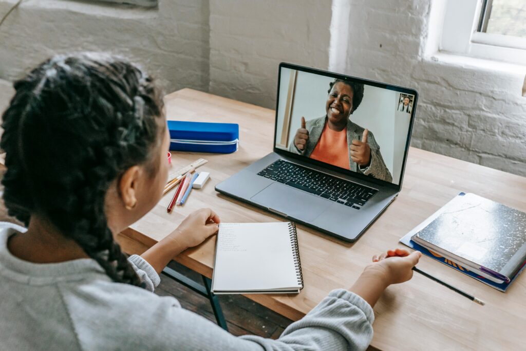a woman sitting at a desk without her face visible, on a video call on her laptop with another woman on the screen