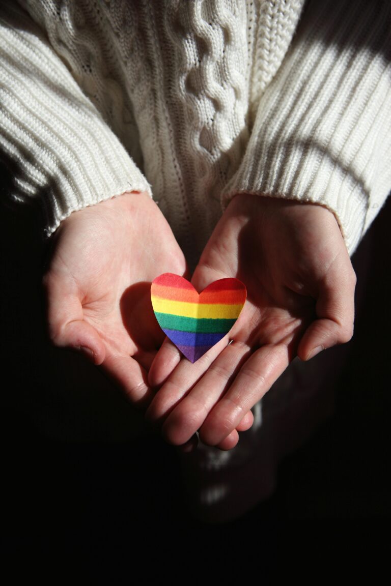 a hand is holding a paper rainbow heart