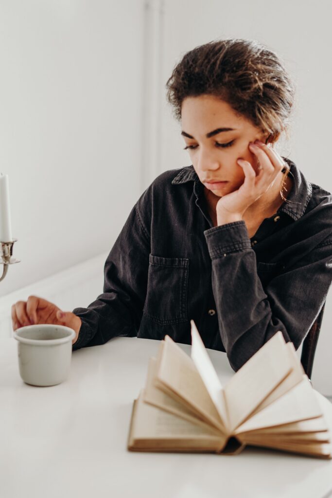 person sitting at a table with an open book and a mug, staring into space