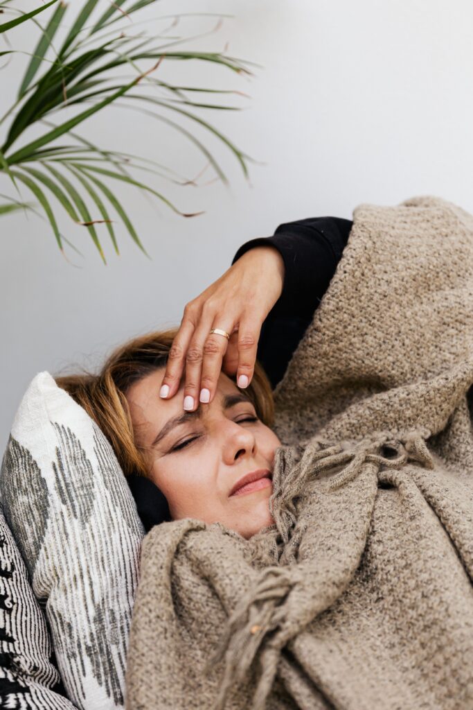 person in bed with her hand on her forehead, wincing