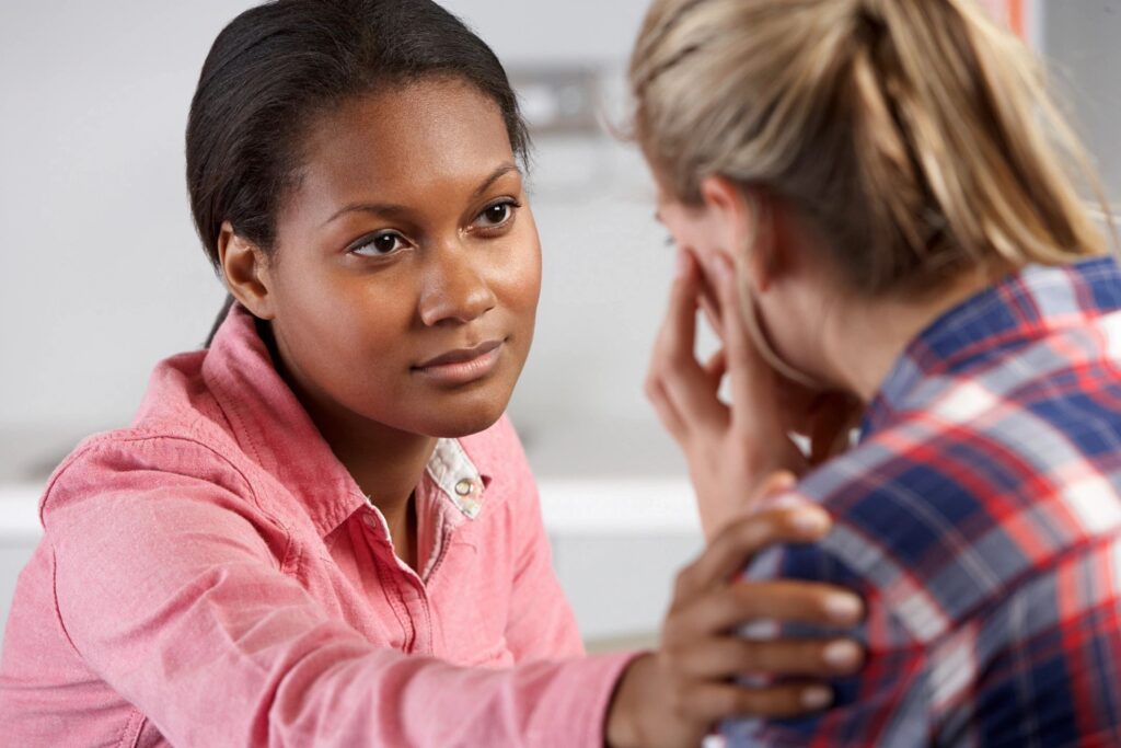 a Black woman gently touching another woman's shoulder and looking at her